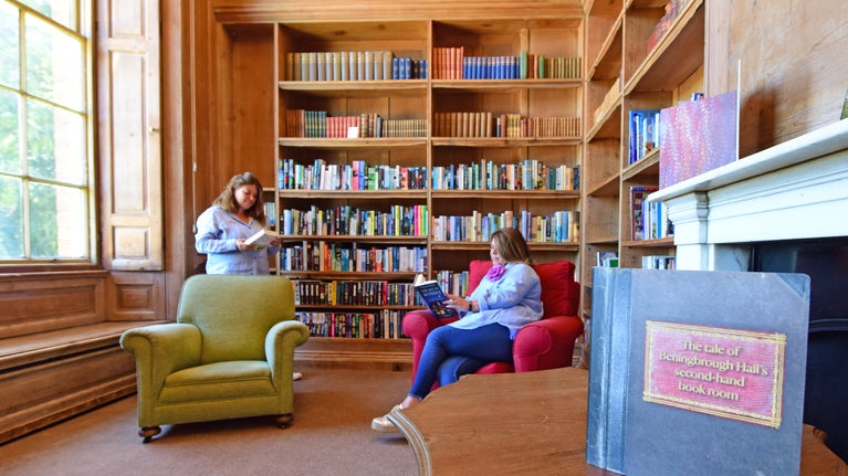 Two women, one standing and one seated, looking at books in a historic library